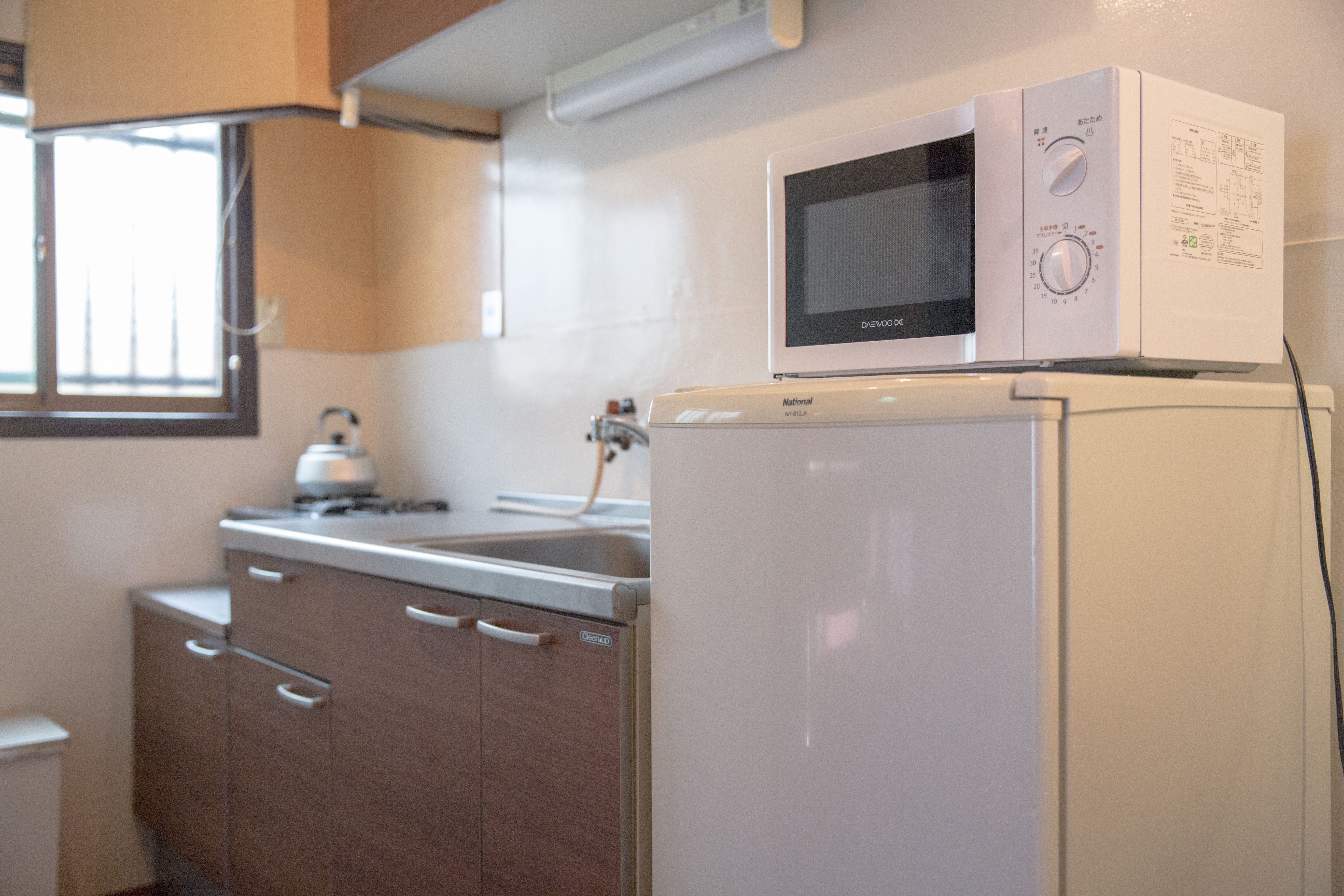 Compact kitchen with dark wood cabinets, stainless steel countertop, gas stove with kettle, and white refrigerator with microwave