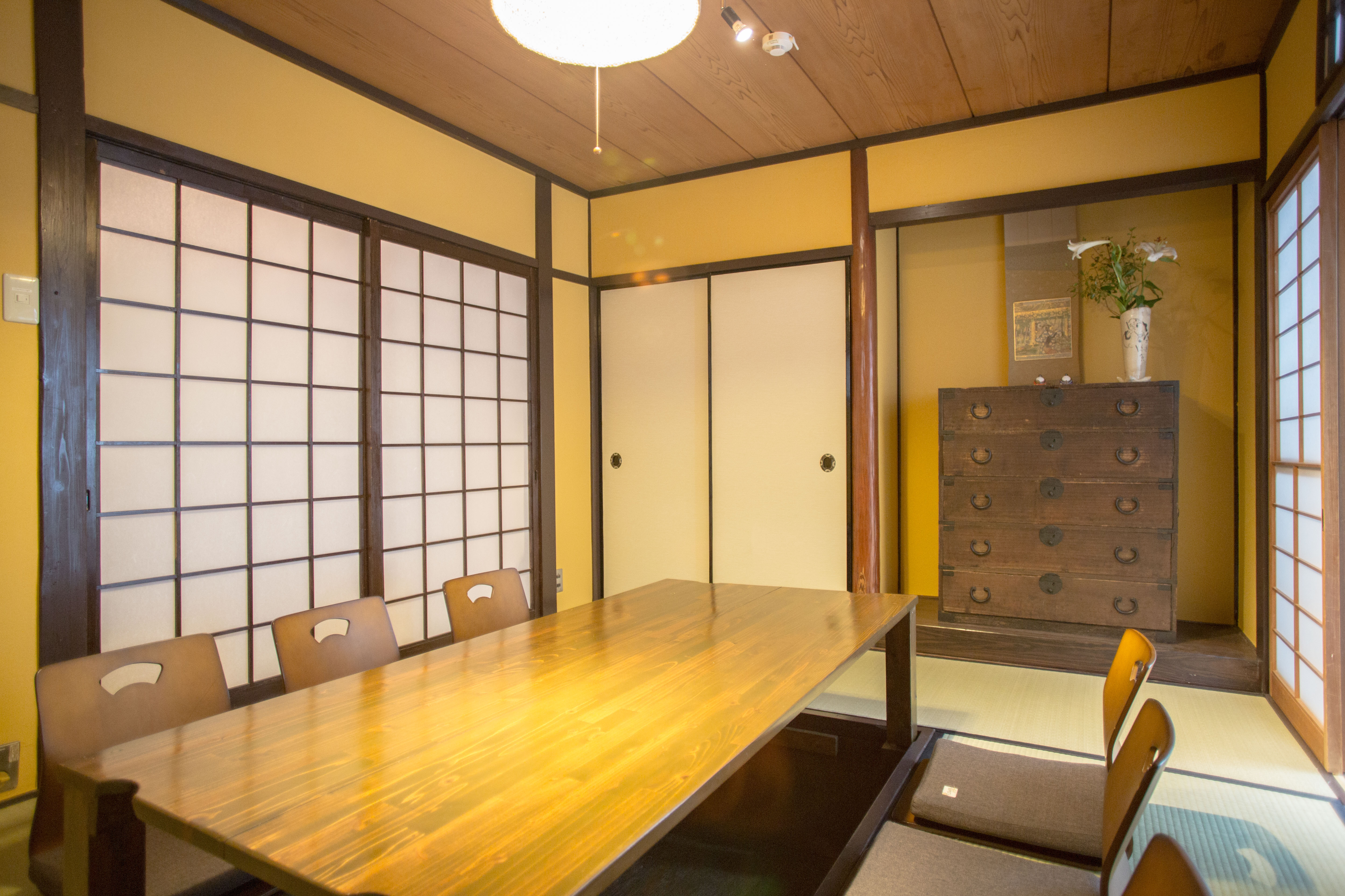 Traditional tatami living room with ochre walls, low dining table with zaisu chairs, antique tansu chest, and shoji screens